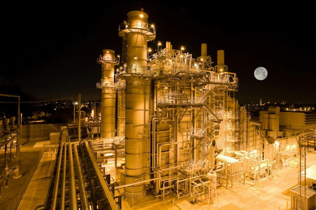 An industrial power plant illuminated at night with a full moon in the sky